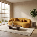 Enzo curved Japandi sofa in gold boucle fabric in a minimalist living room with a low wood coffee table, potted fiddle-leaf fig, and light-filled grid window.