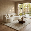 Enzo 89-inch curved Japandi ivory boucle sofa in a minimalist living room, styled with matching pillows on a cream rug, beside a round wooden coffee table and a window looking onto a bamboo garden.