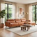 Erika 109-inch cognac PU leather right-facing sectional sofa with chaise lounge set on a textured cream rug in a bright, modern living room with large windows and nested wooden coffee tables.
