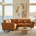 Eugina 92-inch tan genuine leather corner sectional sofa with tapered wooden legs set in a modern sunlit living room with scenic ocean views.
