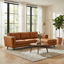Eugina 92-inch tan genuine leather corner sectional sofa with chaise styled in a bright, modern living room with large windows, a round wooden coffee table, patterned area rug, and brass floor lamp.