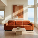 Modern minimalist living room featuring the Franca 107 burnt orange velvet power slider sofa, a travertine stone coffee table, a large earthy abstract painting, and floor-to-ceiling windows overlooking a coastal ocean view.