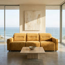 Modern Franca 107 gold velvet power slider sofa in a luxury minimalist living room with floor-to-ceiling windows overlooking the ocean.