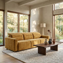 Franca 107 Gold Velvet Power Slider Sofa in a sunlit modern living room with large wood-framed windows, a live-edge dark wood coffee table, and a plush textured rug.