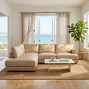 Gamila 110-inch beige genuine top grain leather left-facing sectional sofa styled in a coastal living room with a white marble coffee table, jute rug, fiddle-leaf fig plant, and open French doors showing a scenic ocean view.