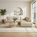 Gamila 110-inch beige genuine top-grain leather right-facing sectional sofa styled with a travertine coffee table and textured rug in a bright, modern living room with an arched wall niche.