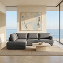 Gamila 110-inch grey fabric left-facing sectional sofa arranged on a neutral area rug in a sunlit modern living room with large ocean-view windows and a stone coffee table.