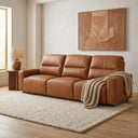 Gina 117 cognac genuine leather power slider sofa in a modern living room, featuring a three-seater design with a beige throw blanket, textured rug, and side table.