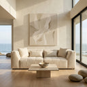 Modern beige chenille sofa, the June 98, styled with matching throw pillows in a bright, minimalist living room with wood floors, a travertine coffee table, abstract art, and floor-to-ceiling windows overlooking the ocean.