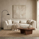 June 98-inch modern beige chenille sofa decorated with matching throw pillows and a beige knit blanket in a minimalist living room, featuring a dark wood coffee table, a textured jute rug, a black arched floor lamp, and a large abstract painting on a beige plaster wall.