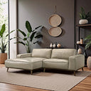 Katia 98-inch beige leather left-facing sectional sofa with wide track arms and tapered wooden legs, set on a neutral woven rug in a modern living room with a dark gray wall, hanging woven baskets, and lush indoor plants.
