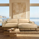 Katia 98-inch beige leather right-facing sectional sofa with chaise and tapered wooden legs in a sunlit modern living room with ocean views.