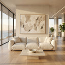 Modern living room featuring the Kely 100 cream boucle upholstered sofa with matching throw pillows, a travertine coffee table, and a large neutral abstract painting, set against floor-to-ceiling windows with a coastal ocean view.