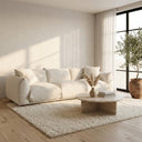 Kely 100 cream boucle upholstered sofa in a minimalist living room, styled with a round travertine coffee table, textured shag rug, potted olive tree, and soft natural sunlight.