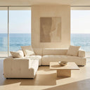 Kendall 120-inch ivory boucle L-shaped sectional corner sofa with grid tufting and matching throw pillows in a sunlit coastal living room with ocean views and a travertine coffee table