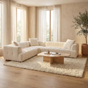 Kendall 120-inch ivory boucle L-shaped corner sectional sofa with channel-tufted cushions and matching throw pillows, styled in a sunlit modern living room with a plush cream shag rug, travertine coffee table, sheer floor-to-ceiling curtains, and an indoor olive tree.