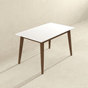 Mid-century modern 47-inch rectangular dining table featuring a smooth white tabletop with beveled edges and four angled, tapered dark brown wooden legs, set against a minimalist textured beige wall and floor.
