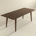 Modern 87-inch dark walnut rectangular dining table featuring a slim beveled tabletop with natural wood grain and four angled, tapered legs, set against a minimalist textured cream wall and floor.
