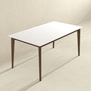 Modern rectangular dining table featuring a smooth white top with softly rounded corners, supported by a sleek dark brown wood frame and four tapered legs, set against a neutral textured beige wall and floor.
