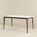 Modern rectangular dining table featuring a sleek white tabletop with gently rounded corners, supported by a dark brown wooden frame and tapered mid-century style legs, set against a neutral textured beige wall and floor.

