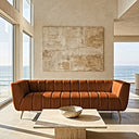 Lorena 86-inch cognac genuine Italian leather sofa with vertical channel tufting and gold legs in a modern minimalist living room overlooking the ocean, featuring a travertine coffee table and abstract canvas art.