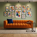 Mia 90-inch mid-century modern orange velvet sofa with vertical channel tufting in a living room. The sofa features a navy blue pillow and sits next to a black C-shaped side table with a glass top. In the background, a sage green wall is decorated with a gallery wall of colorful abstract framed art under track lighting.