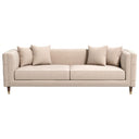 Nina 90-inch mid-century modern beige velvet sofa with four matching throw pillows, featuring vertical stitched detailing on the inner armrests and tapered wooden legs with brass caps, isolated on a white background.