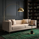 Nina 90-inch mid-century modern beige velvet sofa with channel-tufted details, styled in a moody dark-paneled living room with a brass arc floor lamp, green patterned rug, and marble side table.