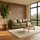 Rita 91-inch olive green top-grain leather sofa styled in a modern living room with an exposed brick wall, a round wooden coffee table, a large potted fiddle-leaf fig tree, and a textured area rug.