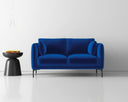 A vibrant dark navy velvet loveseat shown in a minimalist white room, styled with a small black side table and a hanging glass pendant light.