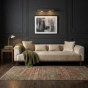 Rosa 103 cream velvet sofa with matching cushions and an olive green throw blanket in a living room with dark charcoal paneled walls, a vintage-style patterned rug, dark hardwood floors, and framed abstract art.