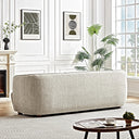 Rear view of the Stacey cream luxury fabric sofa featuring a curved back and low wooden legs in an elegant living room with white paneled walls and a patterned rug.
