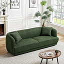 Stacey 87-inch green luxury fabric sofa with curved silhouette and matching throw pillows, styled in a bright living room with a coffee table and geometric rug.
