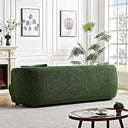 Back view of the Stacey 87-inch green luxury fabric sofa set in a bright, elegant living room featuring white paneled walls, a fireplace, indoor greenery, and a round coffee table on a geometric rug.
