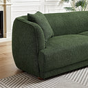 Close-up side view of a dark green textured fabric sofa featuring curved armrests, a matching accent pillow, and short wooden legs on a geometric rug.
