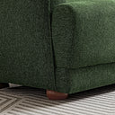 Close-up of the Stacey green fabric sofa showing detailed woven fabric upholstery, cushioned armrest, and a rounded wooden foot on a patterned rug.
