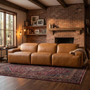 Valeria 120 Triple Power Tan Leather Recliner Sofa in a rustic living room with a red brick fireplace, wooden mantel, and patterned area rug.
