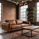 Vanessa 89-inch tan genuine top-grain leather sofa in an industrial-style living room featuring an exposed brick wall, large grid windows, a rustic wooden coffee table, and a patterned area rug.