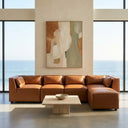 Wanda 93-inch cognac brown vegan leather modular sectional sofa with a right-facing chaise, styled in a sunlit oceanfront living room with an abstract painting and travertine coffee table.