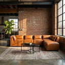 Wanda 93-inch cognac vegan leather modular sectional sofa with right-facing chaise, styled on a vintage patterned rug with black nesting coffee tables in a sunlit industrial loft living room with exposed brick walls.